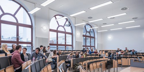 Gut sehen bei der Vorlesung Große bodentiefe Fenster lassen viel Tageslicht in den Höhrsaal. Längs zu ihnen sind Pendelleuchten montiert, die eine blend- und schattenfreie Atmospäre schaffen. Wandleuchten ergänzen die Allgemeinbeleuchtung.